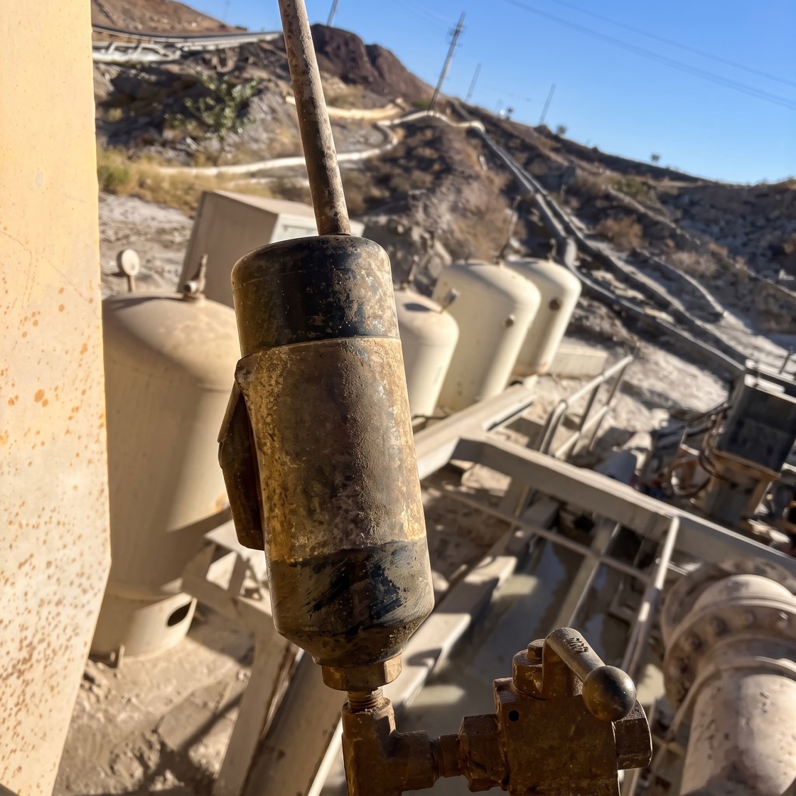 A rugged, unbranded wireless water-pressure sensor with a slim antenna, clamped to steel pipework at a remote mine water facility