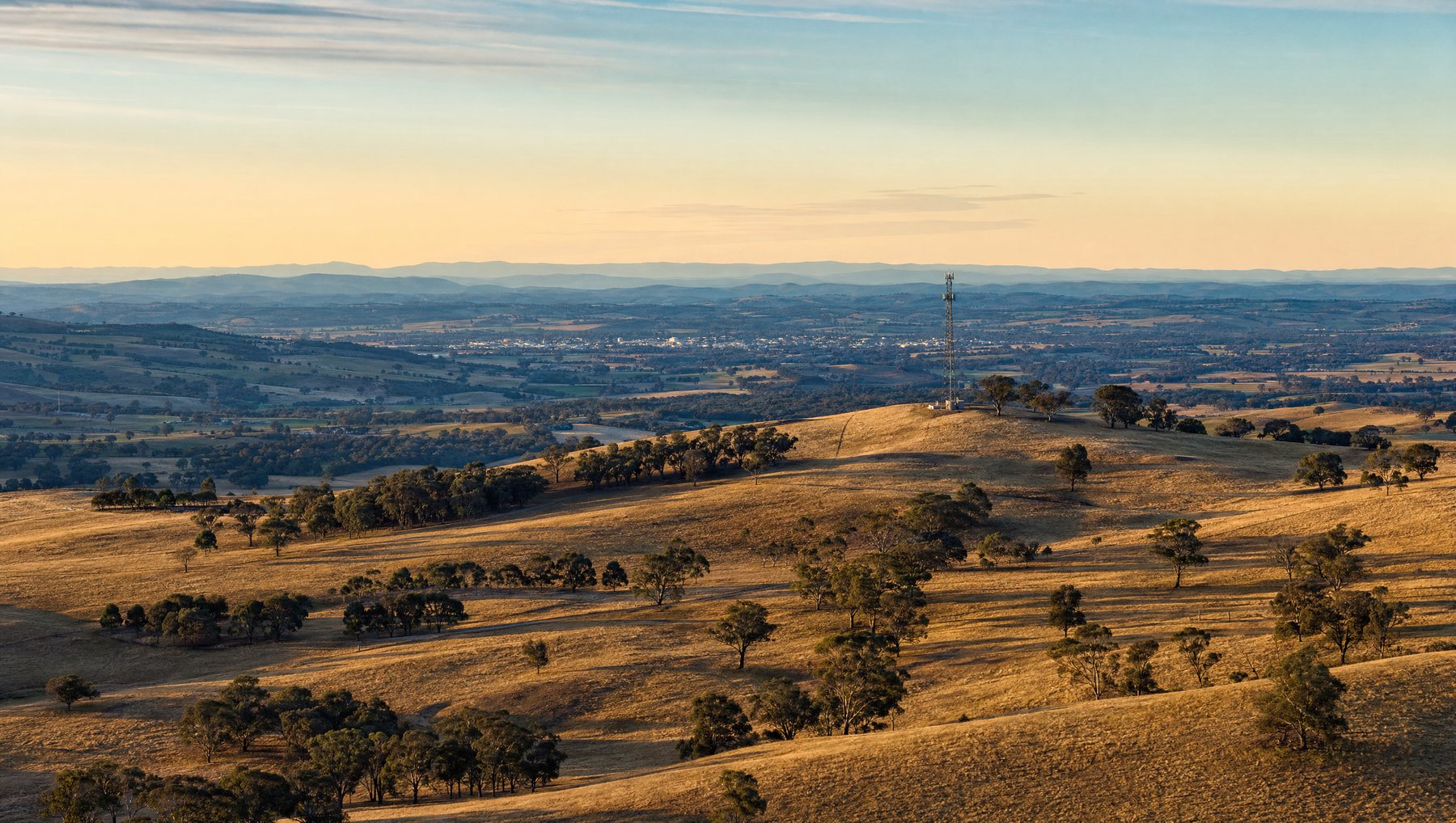 A communications mast on a ridge above rolling golden farmland at sunset