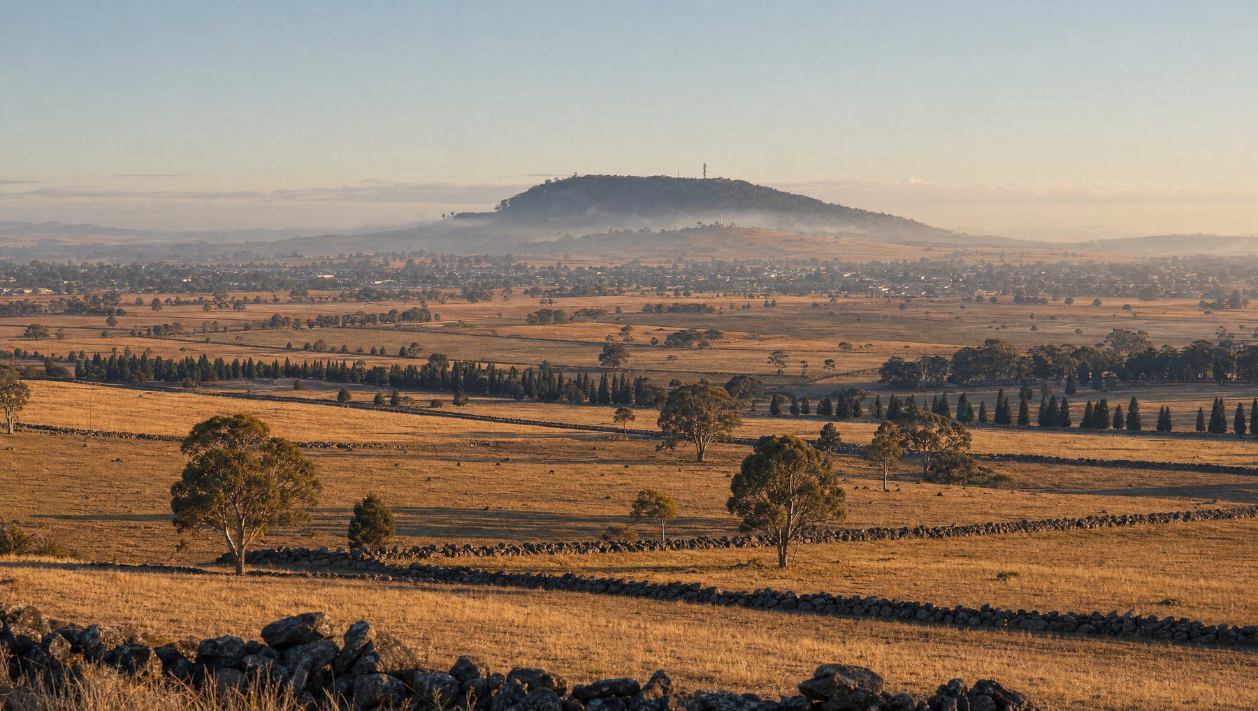 Rolling Victorian farmland at golden hour with a communications mast on a ridge and a country town in the valley beyond