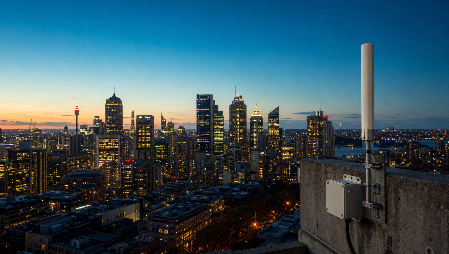 A rooftop antenna and weatherproof enclosure above a city skyline at dusk