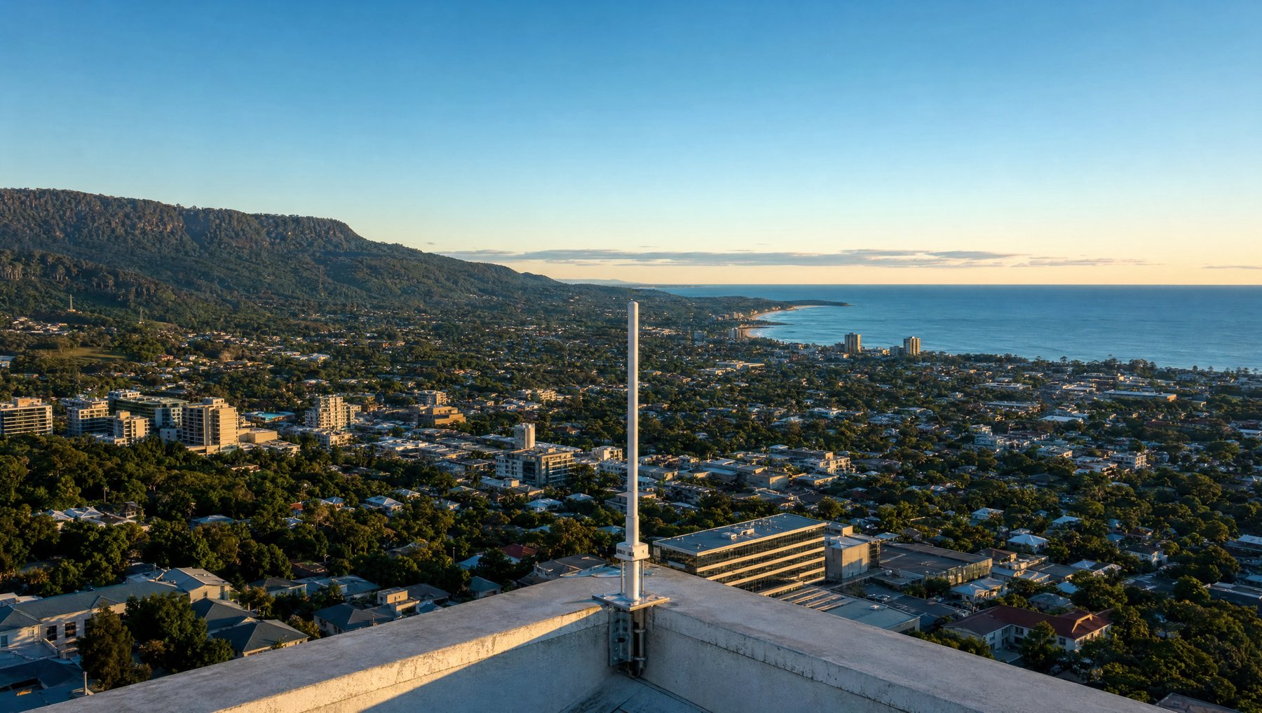 A slim antenna mast on a rooftop parapet overlooking a coastal city