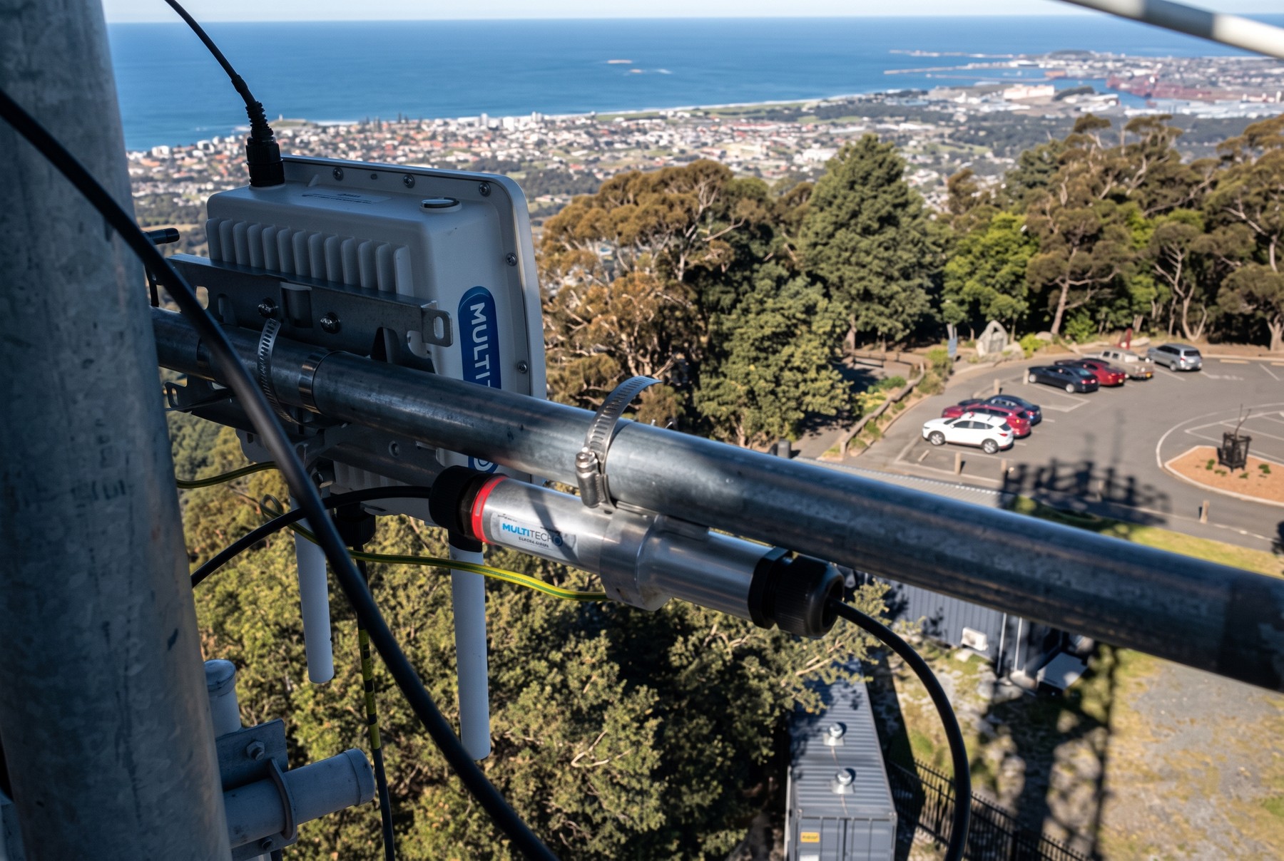 A LoRaWAN gateway and antenna mounted on a mast on high ground, overlooking a regional town and coastline below