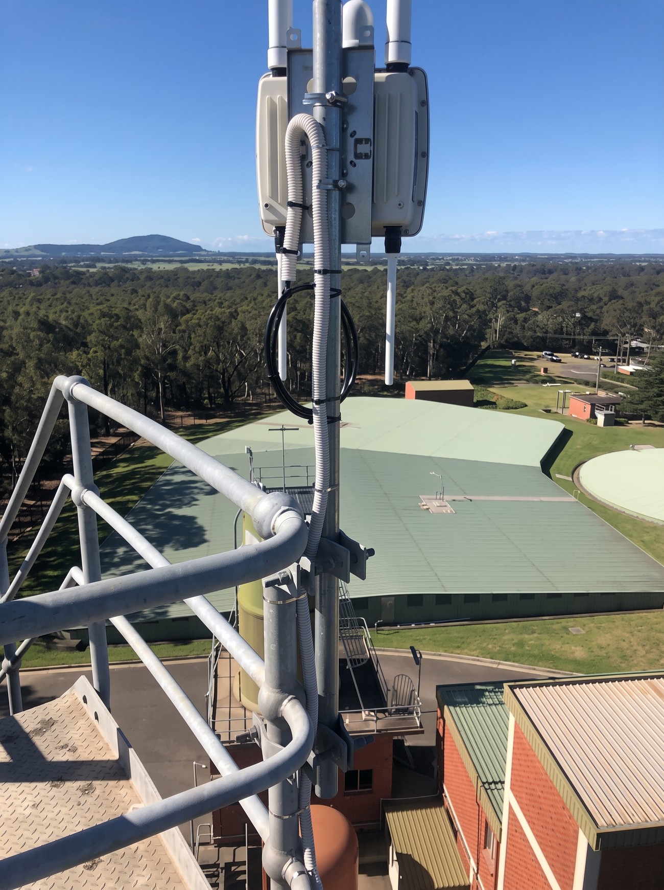 A LoRaWAN gateway with antennas mounted on a mast and handrail above a water reservoir and treatment works, with hills in the distance