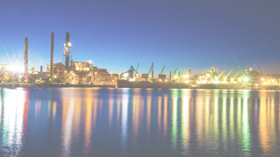 An Australian industrial port working through the night, wharf cranes and ship loaders lit along the berths with the lighting reflected across the harbour