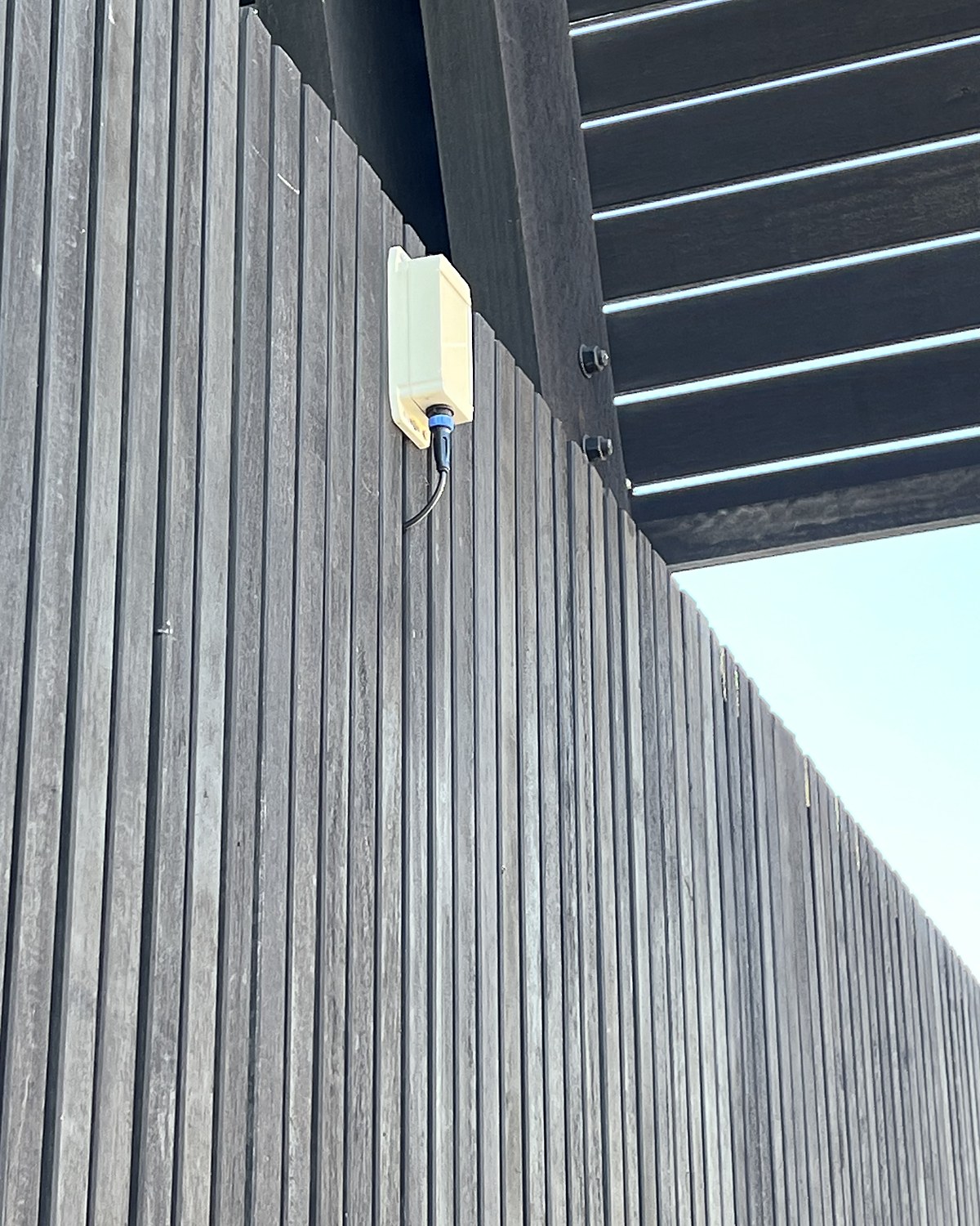 Close view of a small cream nCounter enclosure fixed to a dark timber batten wall beneath a building soffit