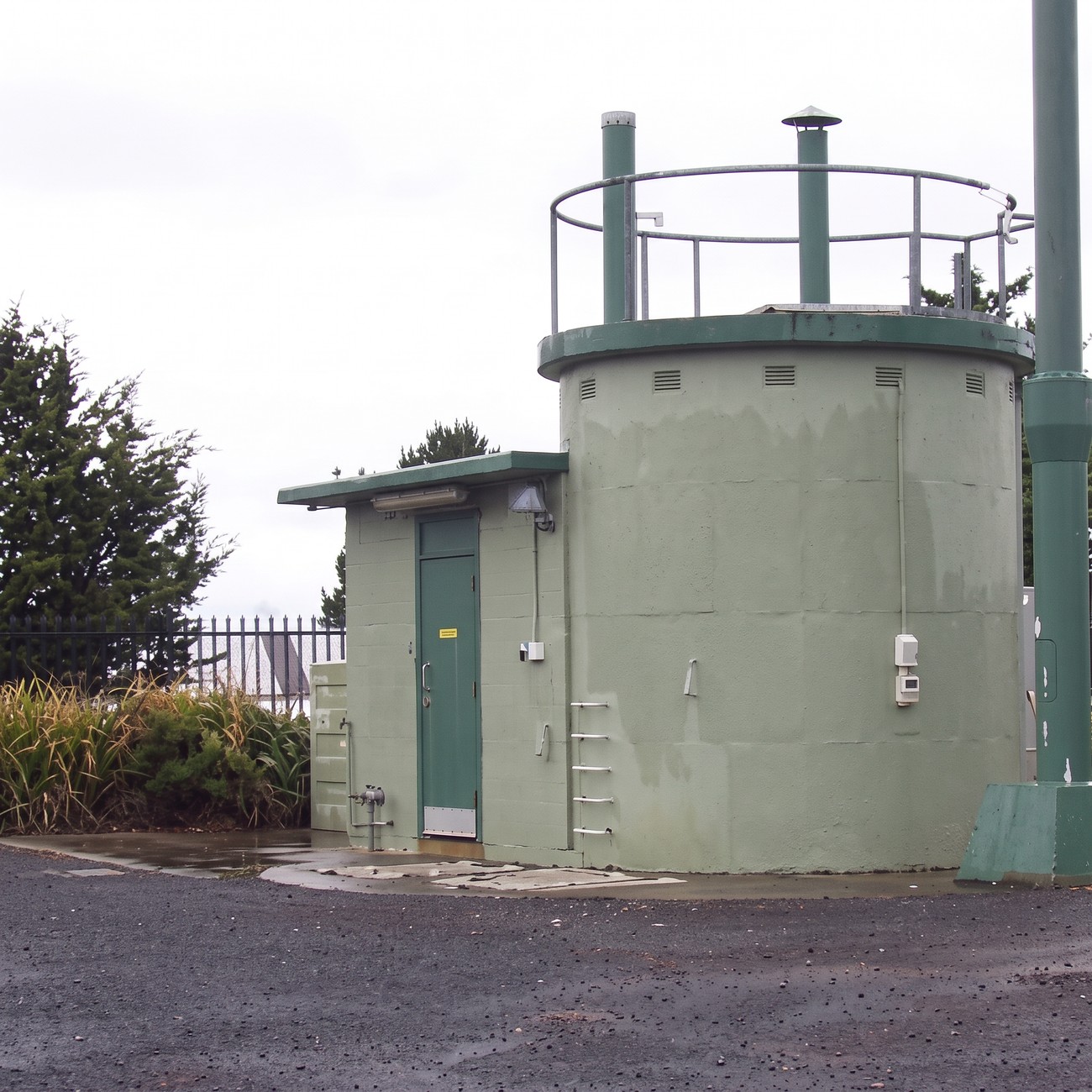 A concrete reservoir and pump station structure with a steel access ladder and handrail platform on top