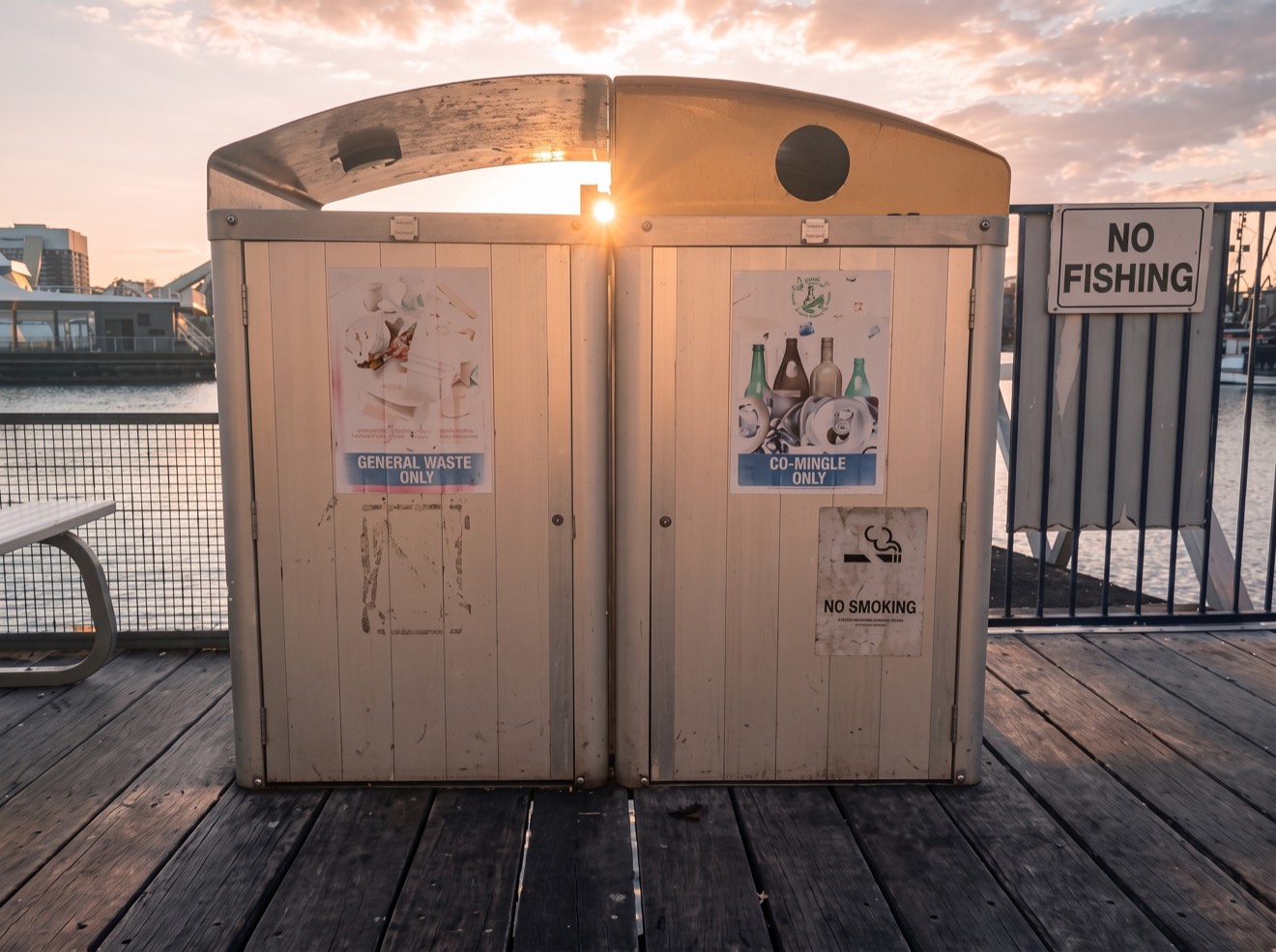 Two public waste and recycling bin enclosures on a Sydney Fish Market harbour wharf at sunset, the assets fitted with bin-level sensors in the pilot