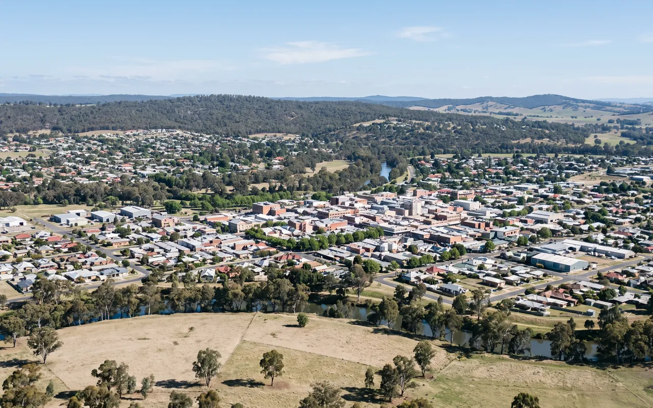 An elevated view over an Australian regional city, its centre and suburbs spread along a tree-lined river with eucalypt hills behind.
