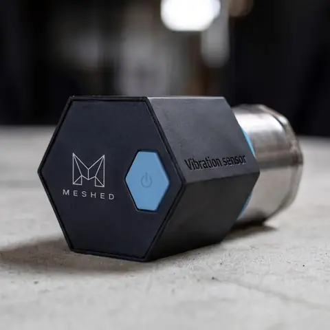 A Meshed wireless vibration sensor, a dark hexagonal body on a steel mounting stud.